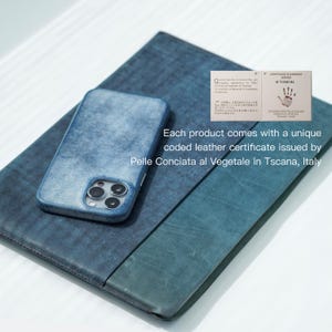 May include: A blue leather phone case and a matching folio are displayed on a light surface. The phone case is on top of the folio. The text on the image says, "Each product comes with a unique coded leather certificate issued by Pelle Conciata al Vegetale in Tscana, Italy."