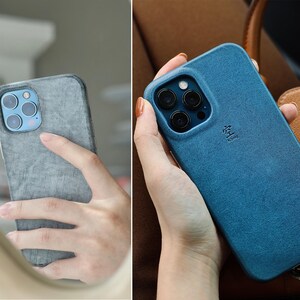 May include: Two images of a smartphone in a textured case. One case is gray, the other is blue. The phone has a multi-lens camera. The blue case has a small symbol and text. The phone is held in a hand.