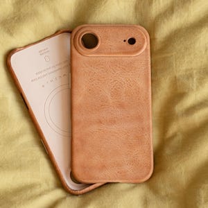May include: A light brown leather phone case with a matching interior. The case has a textured surface and a cutout for the camera. The interior has the text "WUZHI" and other text. The case is lying on a yellow surface.
