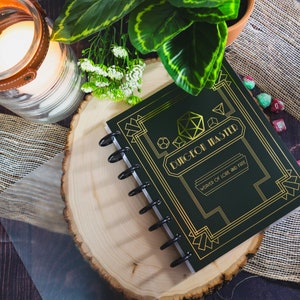 May include: A black and gold spiral bound notebook with the text "Dungeon Master Weaver of Lore and Fate" on the cover.
