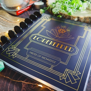 May include: A dark blue notebook with gold accents and the text "LOREKEEPER Master of Knowledge". The notebook has a spiral binding and a decorative design.