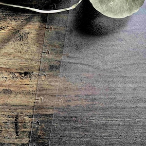 May include: A close-up of a wood grain surface with a piece of clear plastic with a series of holes along the edge. The plastic is partially covering a dark gray surface.