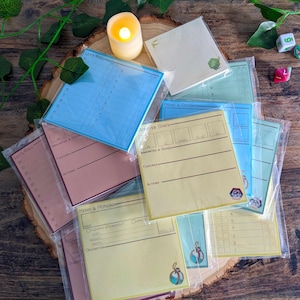 Puede incluir: Un conjunto de ocho blocs de notas adhesivas de color amarillo, azul y rosa con diferentes diseños para juegos de rol. Los blocs tienen títulos como "Let's Roll", "Monster Stats" y "Items & Potions".