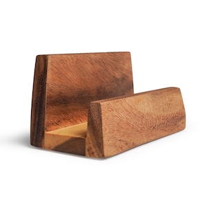 May include: A wooden phone stand with a natural wood grain finish. The stand has a rectangular base and a back support, with a slot to hold a phone. The wood is a warm brown color.