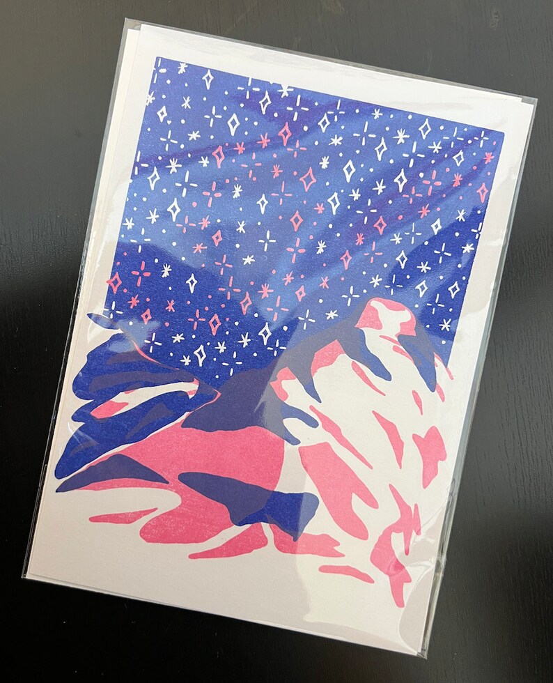May include: A pink and blue abstract print with a white background. The print features a stylized mountain range with a starry sky above.