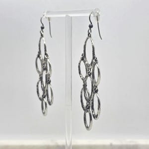 May include: Silver-toned chandelier earrings with multiple oval-shaped links. The earrings have a textured finish and dangle from a simple hook. The design is symmetrical, with each earring featuring a series of connected ovals.
