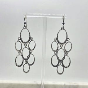 May include: A pair of silver-toned chandelier earrings. Each earring features multiple oval-shaped frames connected in a cascading design. The earrings are displayed against a white background, showcasing their intricate details and vintage style.
