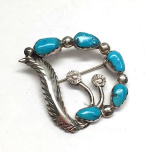 May include: A silver and turquoise brooch with a feather design and a cluster of turquoise stones.