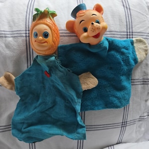 May include: Two vintage hand puppets. One is a smiling pineapple with a green leafy top and blue eyes. The other is a bear wearing a blue hat. Both puppets have blue fabric bodies and tan felt hands.