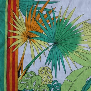 May include: A white textile with a tropical leaf pattern. The design features large green, yellow, and orange palm leaves and other tropical foliage. A vertical stripe with red, orange, and green stripes borders the left side.