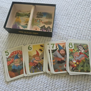 May include: A board game box with a divided interior featuring landscape illustrations and a set of playing cards numbered five through eight. Each card displays colorful artwork of gnomes in garden settings, with the text HOW TO PLAY VIDEO.