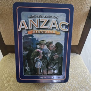 May include: A rectangular, navy blue tin featuring the words "LIMITED EDITION ANZAC BISCUITS" in white and gold lettering. The tin has a painted image of people in front of a ship. The tin contains 500g of biscuits.