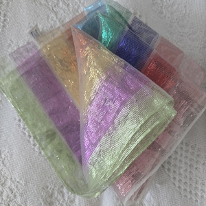 May include: A collection of iridescent, sheer fabric squares in pastel shades. The colours include pink, purple, green, yellow, and blue. The fabric has a shimmering, glittery appearance.