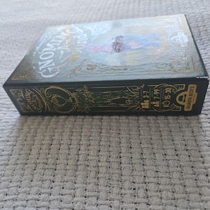 May include: A rectangular board game box titled Gnoming-A-Round with a dark green and gold color scheme. The box features an illustration of a gnome, text details for 3-7 players, ages 7-99, and a 15-30 minute play time by Grandpa Beck's Games.