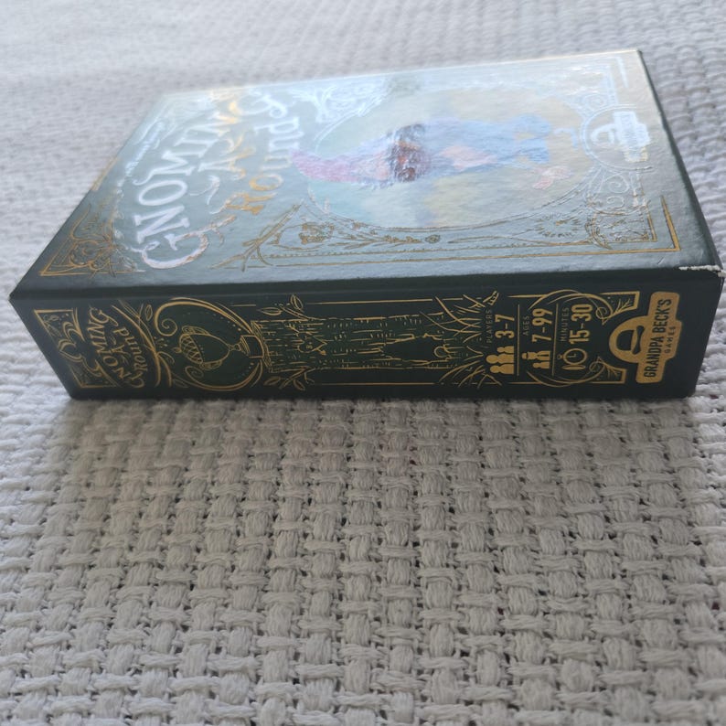 May include: A rectangular board game box titled Gnoming-A-Round with a dark green and gold color scheme. The box features an illustration of a gnome, text details for 3-7 players, ages 7-99, and a 15-30 minute play time by Grandpa Beck's Games.