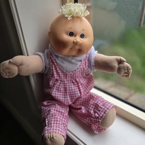 Puede incluir: Una taza de cerámica blanca con asa negra y el texto "But First, Coffee" en negrita negra. La taza se encuentra sobre un fondo borroso, sugiriendo un ambiente acogedor.