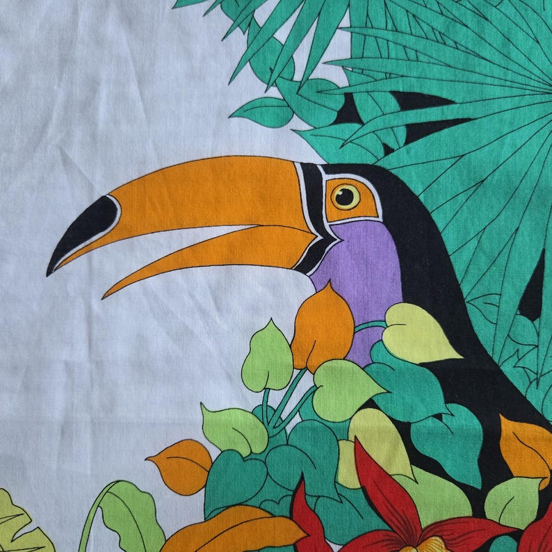 May include: A colorful toucan bird design on a white background, surrounded by green leaves and red and yellow flowers. The toucan has a large orange beak, black head, and purple neck. The design is likely for fabric or a similar textile.