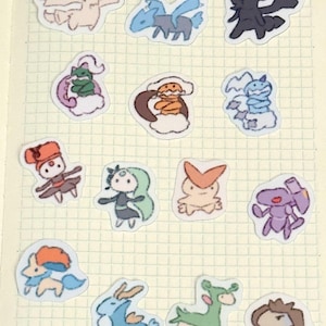 May include: A collection of colorful, cartoon-style stickers featuring various creatures. The stickers are outlined in black and have a variety of colors, including blue, pink, green, orange, and purple. The stickers are placed on a grid-lined paper.