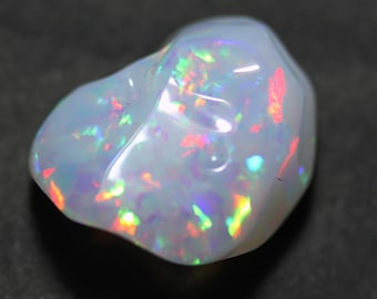 May include: A white opal gemstone with iridescent flashes of color, including red, green, and blue. The opal is irregularly shaped and has a smooth, polished surface.