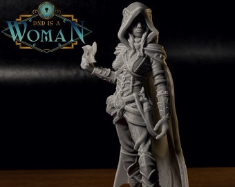 May include: A gray 3D printed miniature of a female figure wearing a hooded cloak and holding a dagger. The figure is standing on a wooden surface.