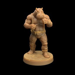 May include: A brown miniature figurine of a hippopotamus-like creature wearing a brown leather belt and pants. The creature has a muscular build and is posed in a fighting stance with its fists clenched.