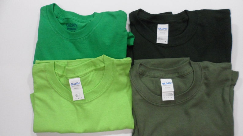 May include: Four folded Gildan brand t-shirts in green, lime green, black, and olive green.
