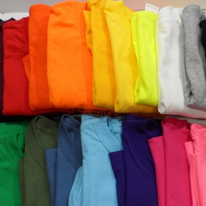May include: A variety of plain t-shirts in different colors, folded and stacked on a white surface.