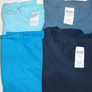 May include: Four folded Gildan brand t-shirts in different shades of blue: light blue, turquoise, denim blue, and navy blue.