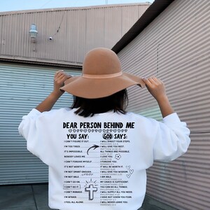 May include: White sweatshirt with a black and white graphic print that says "Dear Person Behind Me You Say: God Says:" with a list of phrases and corresponding bible verses.