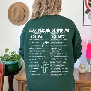 May include: Green sweatshirt with a white print that says "Dear person behind me" and lists encouraging phrases with the words "You say" and "God says".