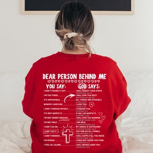 May include: Red sweatshirt with a white graphic print that says "Dear person behind me... You say: I can't figure it out... I'm too tired... It's impossible... Nobody loves me... I can't forgive myself... It's not worth it... I'm not smart enough... I'm not able... I can't go on... I can't do it... I can't manage... I'm afraid... I feel all alone" and "God says: I will direct your steps... I will give you rest... All things are possible... I love you... I forgive you... It will be worth it... I will give you wisdom... I am able... My grace is sufficient... You can do all things... I will supply all you need... I have not given you fear... I will never leave you."