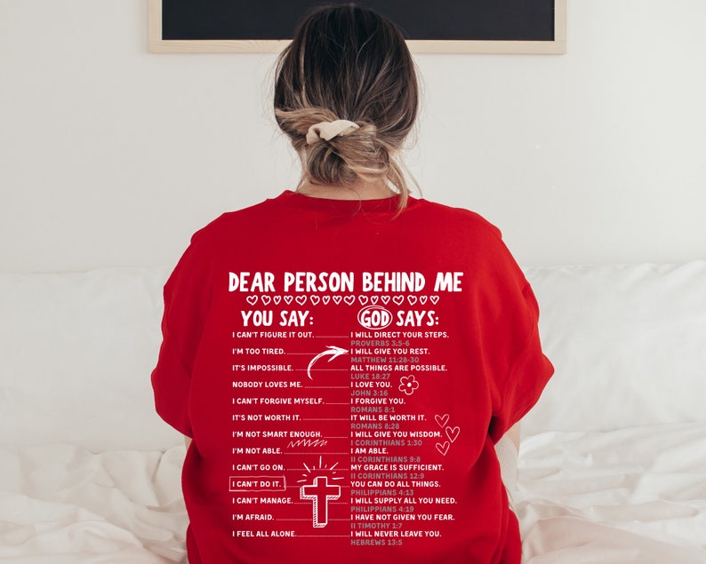 May include: Red sweatshirt with a white graphic print that says "Dear person behind me... You say: I can't figure it out... I'm too tired... It's impossible... Nobody loves me... I can't forgive myself... It's not worth it... I'm not smart enough... I'm not able... I can't go on... I can't do it... I can't manage... I'm afraid... I feel all alone" and "God says: I will direct your steps... I will give you rest... All things are possible... I love you... I forgive you... It will be worth it... I will give you wisdom... I am able... My grace is sufficient... You can do all things... I will supply all you need... I have not given you fear... I will never leave you."