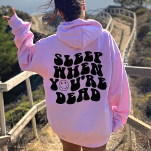 May include: Pink hoodie with a black graphic that says "SLEEP WHEN YOU'RE DEAD" with a smiley face in the middle of the text.