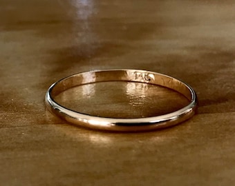 Może przedstawiać: Cienki, polerowany złoty pierścionek w formie obrączki o gładkiej, zaokrąglonej powierzchni. Wewnątrz metalowej obrączki znajduje się wyraźny grawerunek o treści 14K, określający próbę złota tego wyrobu jubilerskiego.