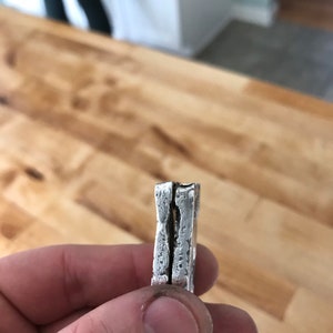 Puede incluir: Un anillo de plata con una superficie gruesa, texturizada e irregular. La banda presenta una hendidura vertical distintiva en el centro, creando una apariencia de doble capa con un acabado rugoso similar al martillado en los bordes.
