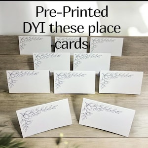 May include: A set of white rectangular place cards arranged in rows, each featuring a black line art floral illustration in the top left corner. The text Pre-Printed DYI these place cards is displayed above the cards in a simple black font.