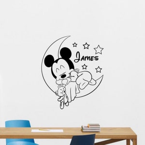 Peut inclure: Illustration en noir et blanc d'un bébé Mickey Mouse dormant sur un croissant de lune avec un ours en peluche. Le nom "James" est écrit au-dessus de la lune.