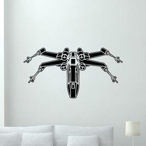May include: Black and white graphic of an X-wing starfighter. The image shows the iconic spacecraft from a top-down perspective, with its distinctive wings and cockpit clearly visible. The design is a minimalist, silhouette style.