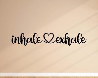 Puede incluir: Texto negro en cursiva sobre una pared beige que dice "inhale exhale" con un símbolo de corazón que conecta las palabras. El texto está centrado sobre un suelo de madera, creando un diseño minimalista.