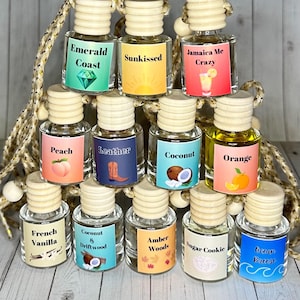 May include: A collection of ten small glass bottles with wooden tops and colorful labels. Each bottle has a different scent, including Emerald Coast, Sunkissed, Jamaica Me Crazy, Peach, Leather, Coconut, Orange, French Vanilla, Coconut & Driftwood, Amber Woods, Sugar Cookie, and Ocean Breeze.