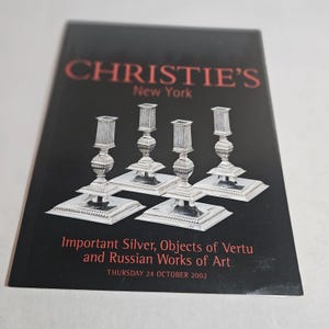 May include: A black catalog cover with the Christie's New York logo in red. The catalog features four silver candlesticks. Text reads "Important Silver, Objects of Vertu and Russian Works of Art" and "THURSDAY 24 OCTOBER 2002."