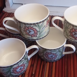 Op de afbeelding: Set van zes witte keramische soepmokken met een bloemenmotief in roze, groene en bruine tinten. De mokken hebben een ronde vorm en een handvat aan de zijkant.