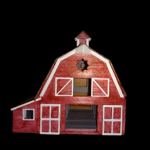Könnte beinhalten: Ein rotes Holzmodell einer Scheune mit weißen Verzierungen und einem kleinen Fenster im Dach. Die Scheune hat zwei große Türen und ein kleineres Fenster an der Seite.