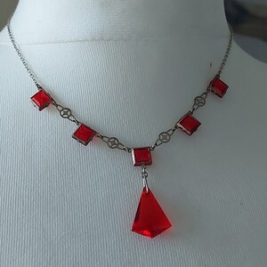 May include: A silver chain necklace with a red teardrop pendant and red square-shaped stones.