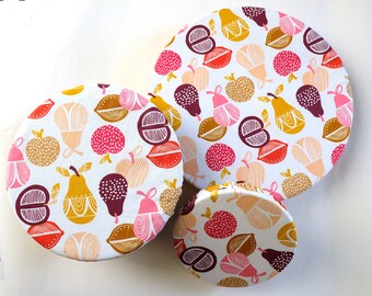 May include: Three reusable food wraps with a white background and a colorful pattern of pears, apples, and lemons. The wraps are made of fabric and are designed to cover bowls and containers to keep food fresh.