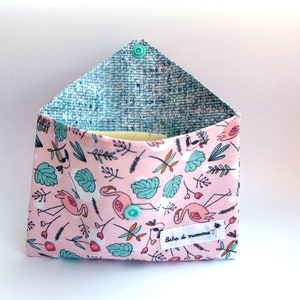 Könnte beinhalten: Rosa Stofftasche mit blau-weiß gemustertem Futter. Die Tasche hat einen Flamingoprint mit grünen Blättern und ein kleines Etikett mit der Aufschrift "Bicho di mamma".