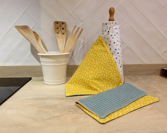 Op de afbeelding: Een set keukendoeken met een geel en wit geometrisch patroon. De doeken zijn gevouwen en worden getoond op een aanrecht met een witte keramische bestekhouder en houten keukengerei.