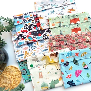 Puede incluir: Una colección de bolsas rectangulares de tela para aperitivos con varios patrones coloridos que incluyen piratas, helicópteros, zorros con el texto be wild, corazones, unicornios y paraguas. Cada bolsa se cierra con dos botones de presión.