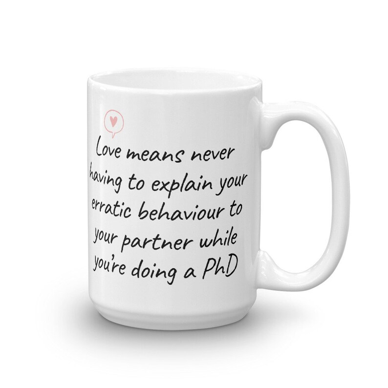 Puede incluir: Taza de caf&eacute; de cer&aacute;mica blanca con un mensaje escrito a mano en negro que dice "El amor significa no tener que explicar nunca tu comportamiento err&aacute;tico a tu pareja mientras haces un doctorado".