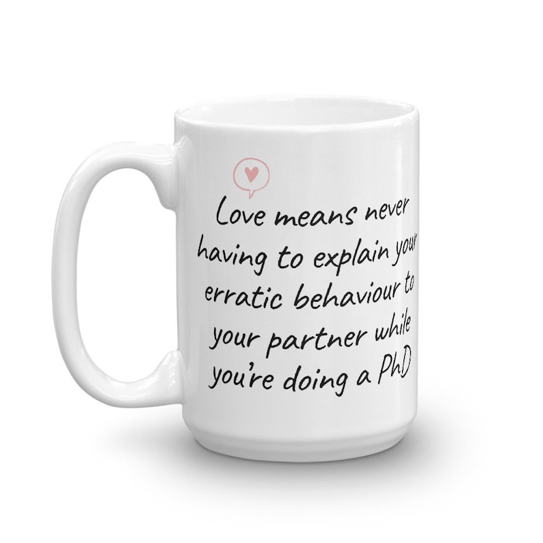 Puede incluir: Taza de cer&aacute;mica blanca con una cita manuscrita en negro que dice "El amor significa no tener que explicar nunca tu comportamiento err&aacute;tico a tu pareja mientras haces un doctorado".